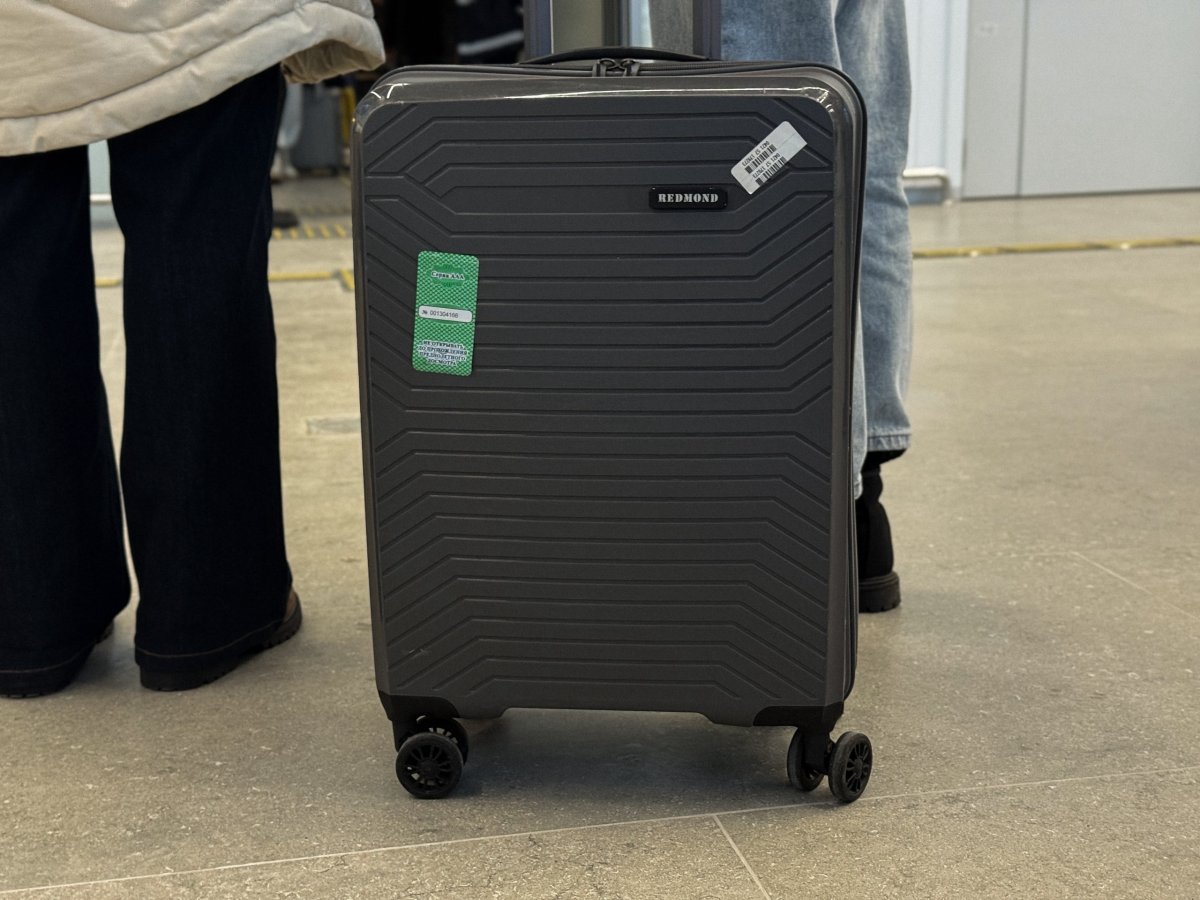 Ноги в брюках и рядом чемодан на колесах.