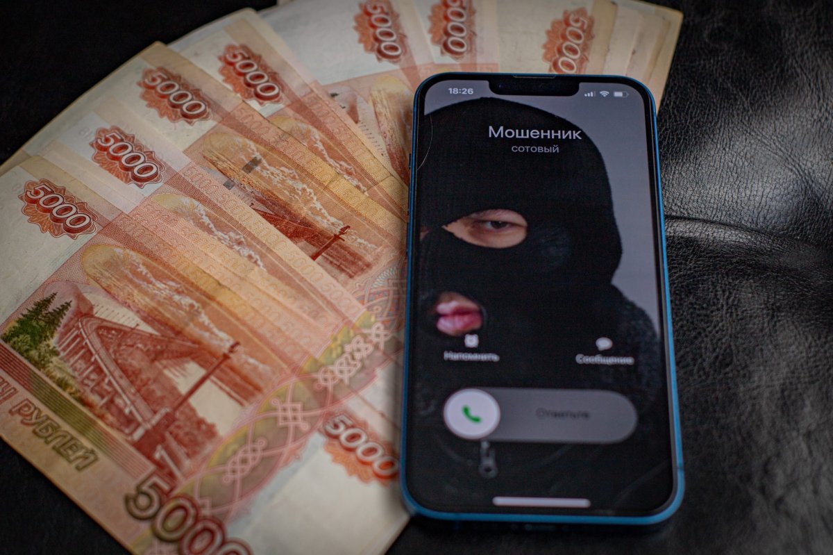 Денежные купюры и мобильный телефон с изображением мошенника в маске