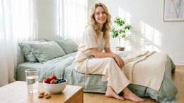 Женщина сидит на кровати в освещенной спальне.