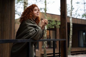 Девушка укуталась в плед и стоит на террассе.