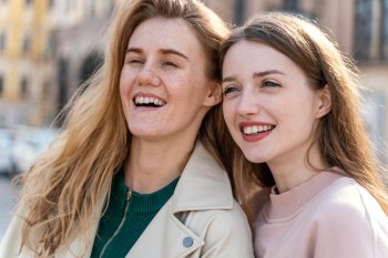 Две девушки смеются, позируя на улице.