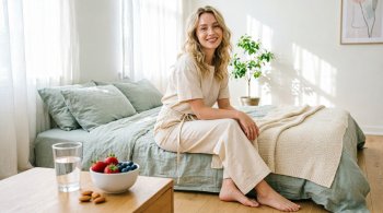 Женщина сидит на кровати в освещенной спальне.